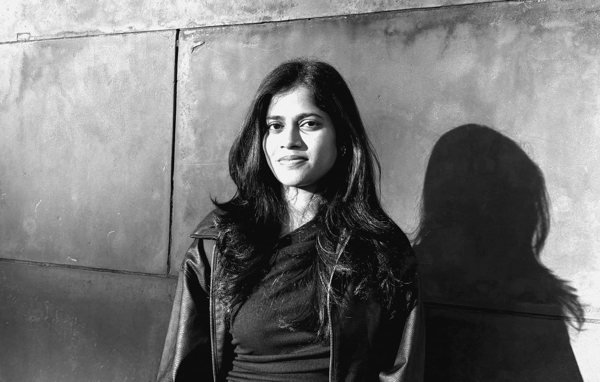 Snehal Shinde standing against a sunlit wall, her shadow beside her